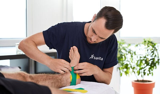 Ein junger Therapeut klebt ein Kinesiotape auf den Fuß eines Mannes.