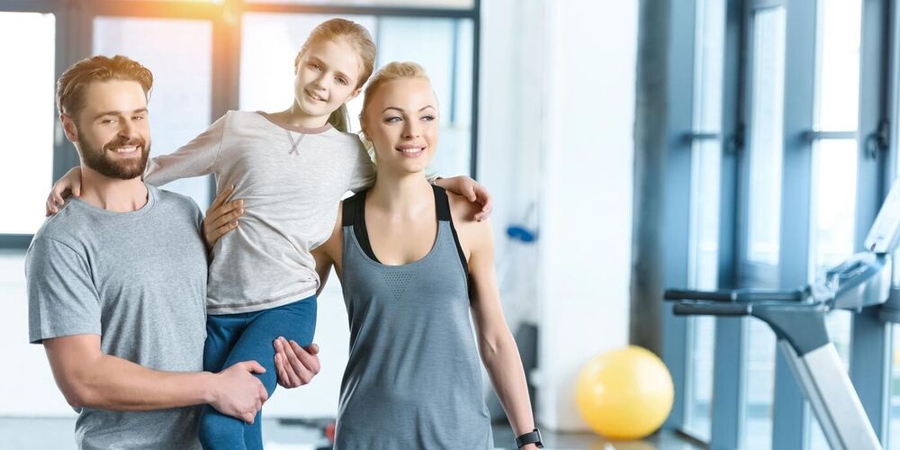 Familie im Fitnessstudio: Mutter, Vater und junges Mädchen in sportlicher Kleidung