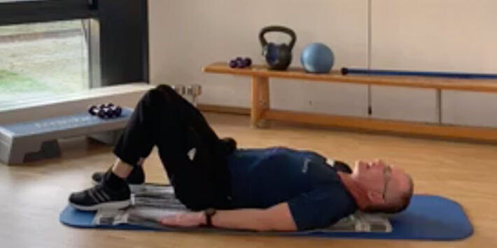 Fitnesstrainer macht Übung vor: Er liegt mit angewinkelten Beinen auf dem Rücken.