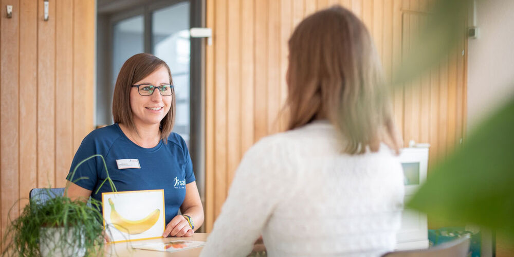 Logopädin zeigt der Patientin eine Karte mit einer Banane und übt mit ihr die Aussprache