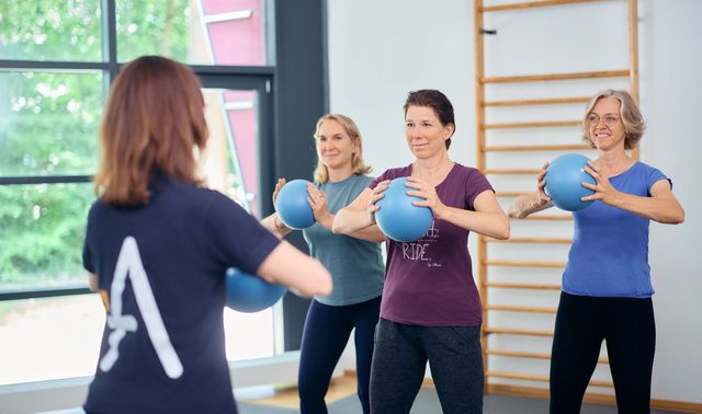 Drei Frauen trainieren beim Rehasport im Therapie- und Trainingszentrum Neuss mit blauen Gymnastikbällen unter Anleitung einer Trainerin.