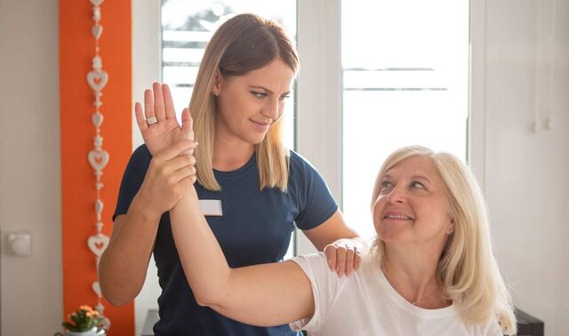Physiotherapeutin hält den Arm einer Patientin in der Hand und bewegt diesen.
