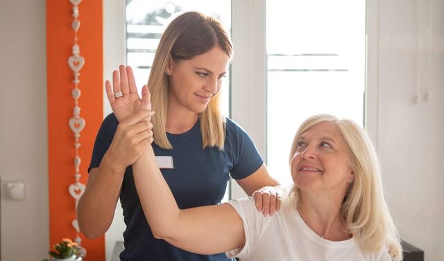 Physiotherapeutin hält den Arm einer Patientin in der Hand und bewegt diesen.