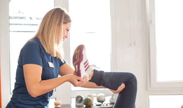Eine Physiotherapeutin hält das Bein einer Patientin in der Hand und beugt es.
