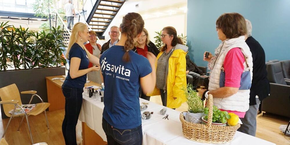 Bild vom Stand der savita mit zwei Mitarbeiterinnen. Davor stehen eine Vielzahl interessierte Besucher, die an Lebensmitteln und Gläsern schnuppern.